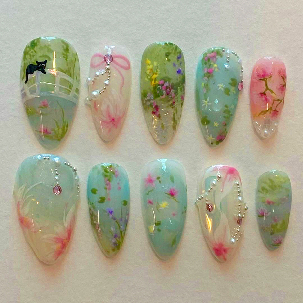 A set of long almond-shaped nails with pastel colors featuring floral designs and gemstone accents.