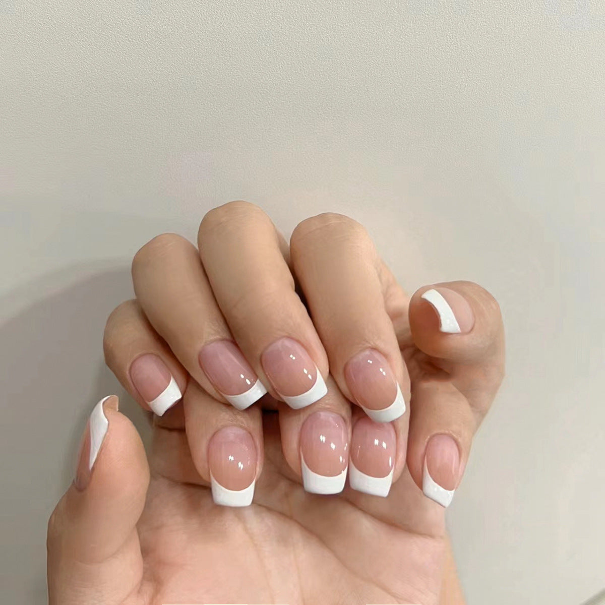 Hand with nails featuring a French manicure design on a neutral background