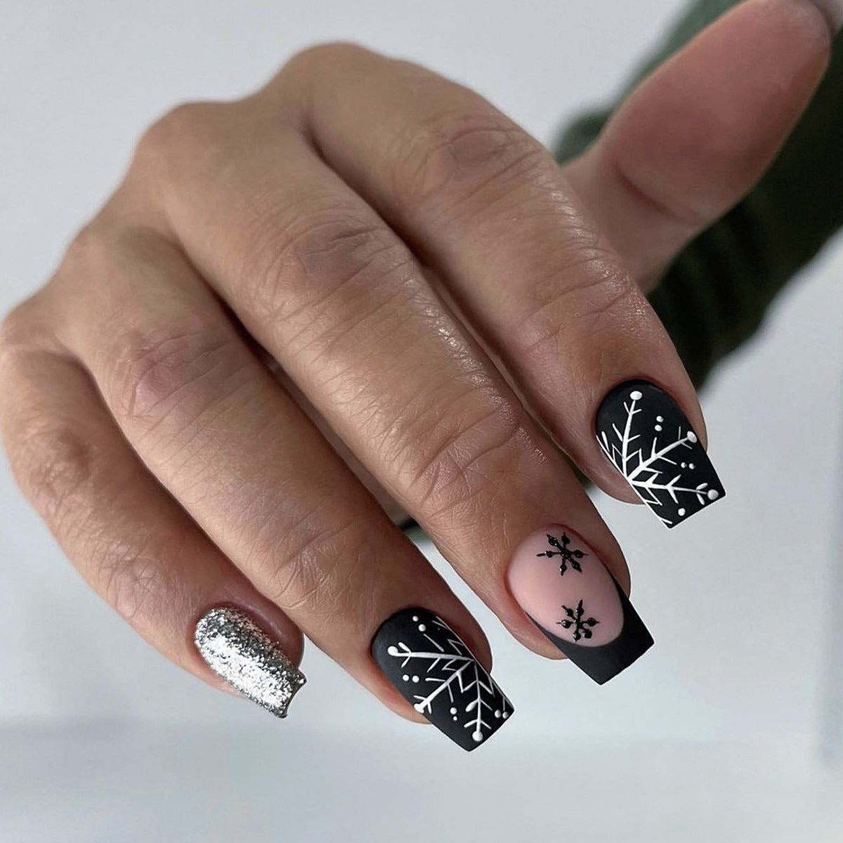 A set of press-on nails featuring a snowflake design with black and pink coloring and a sparkling accent nail.