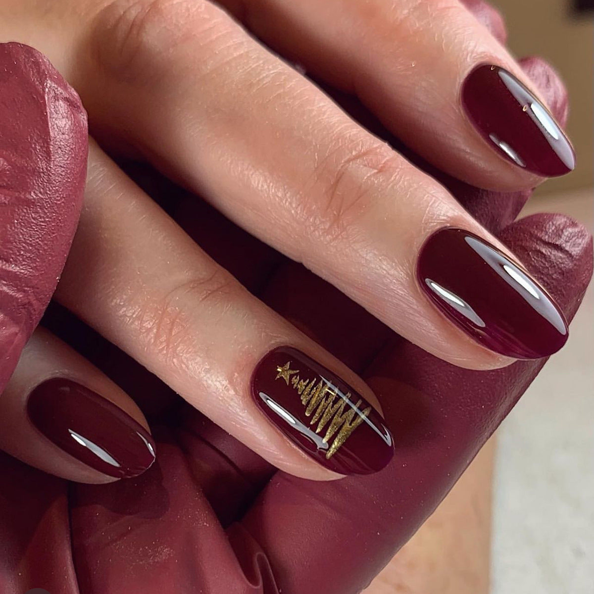 Close-up of a hand with dark red nail polish and gold star design.