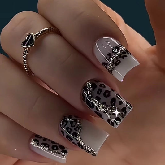 A set of beige and black leopard print nails with glitter accents, displayed on a hand.