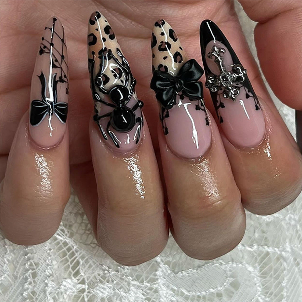 A set of long stiletto nails featuring black and beige design with unique spider and bow accents on a glossy background.