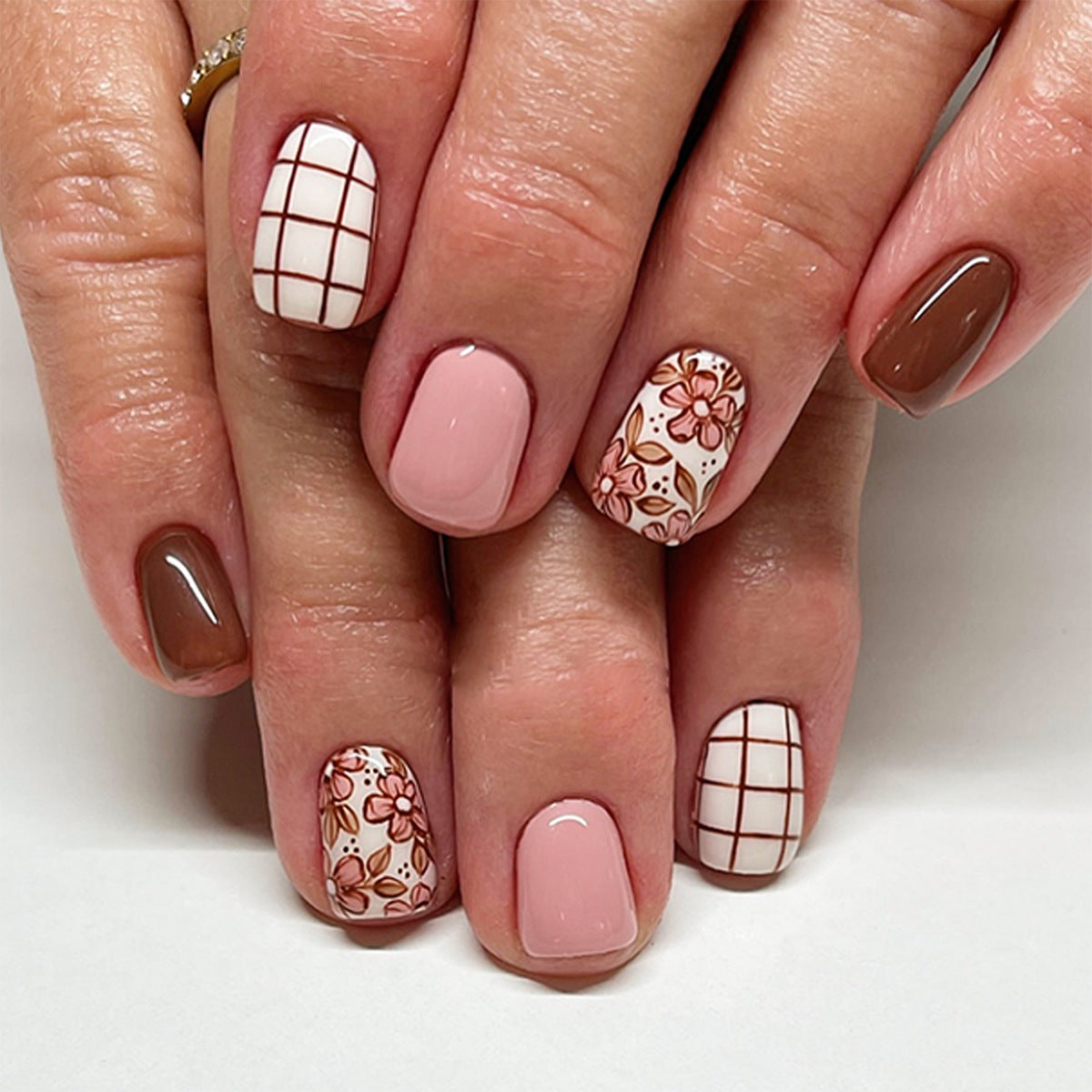 Close-up of a hand with brown and pink nail designs on a white background