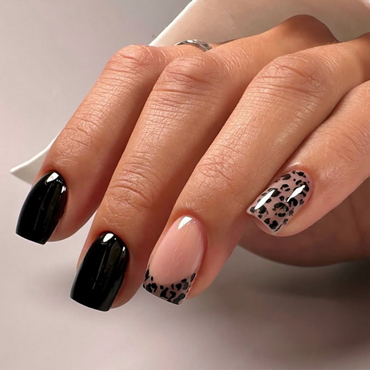 Close-up of a hand with black and leopard print nail designs on a neutral background