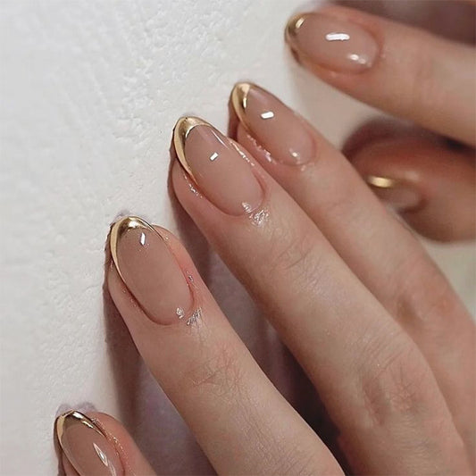 Close-up of a hand with beige nail polish and gold tips on a white background