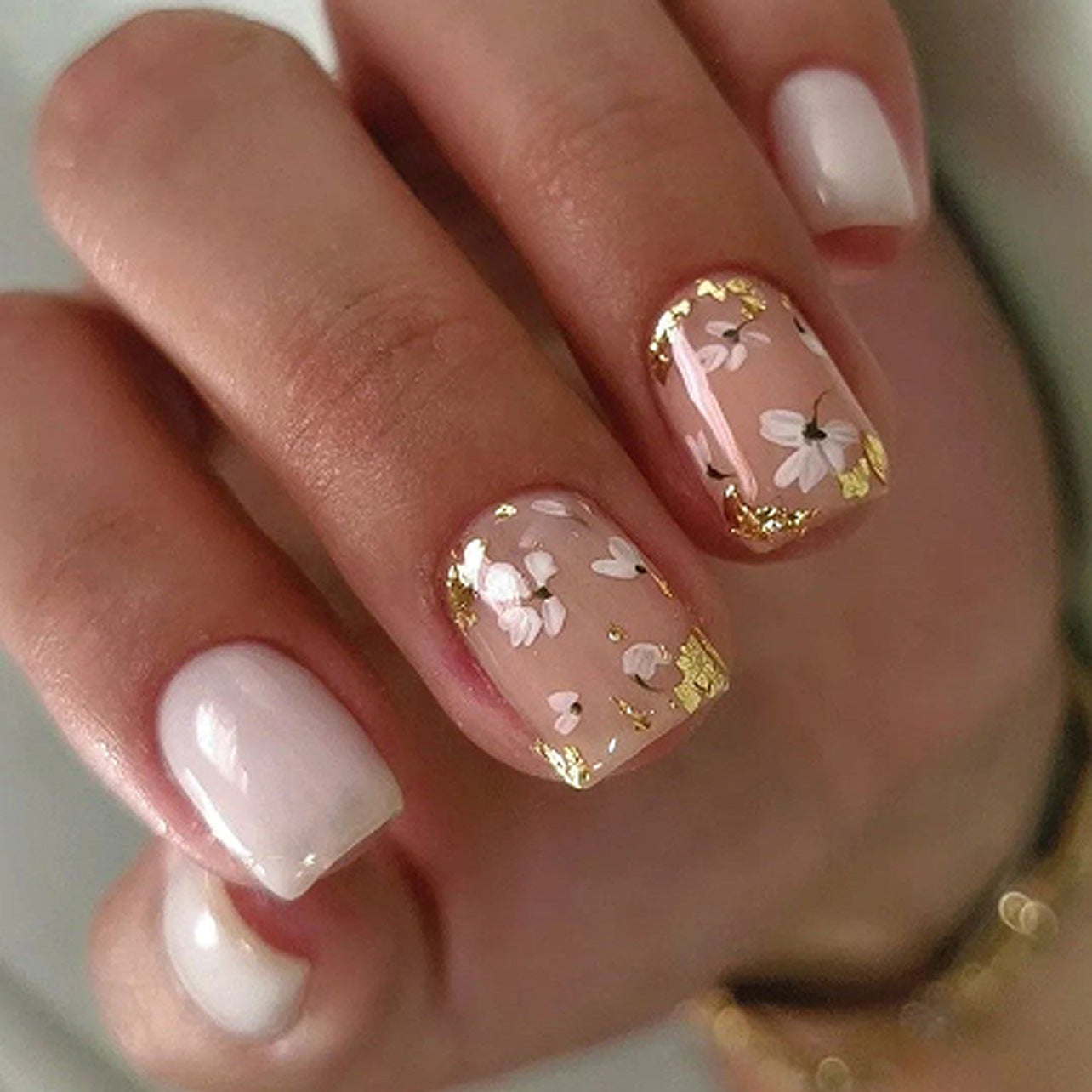 Close-up of a hand with pink and gold floral nail design.