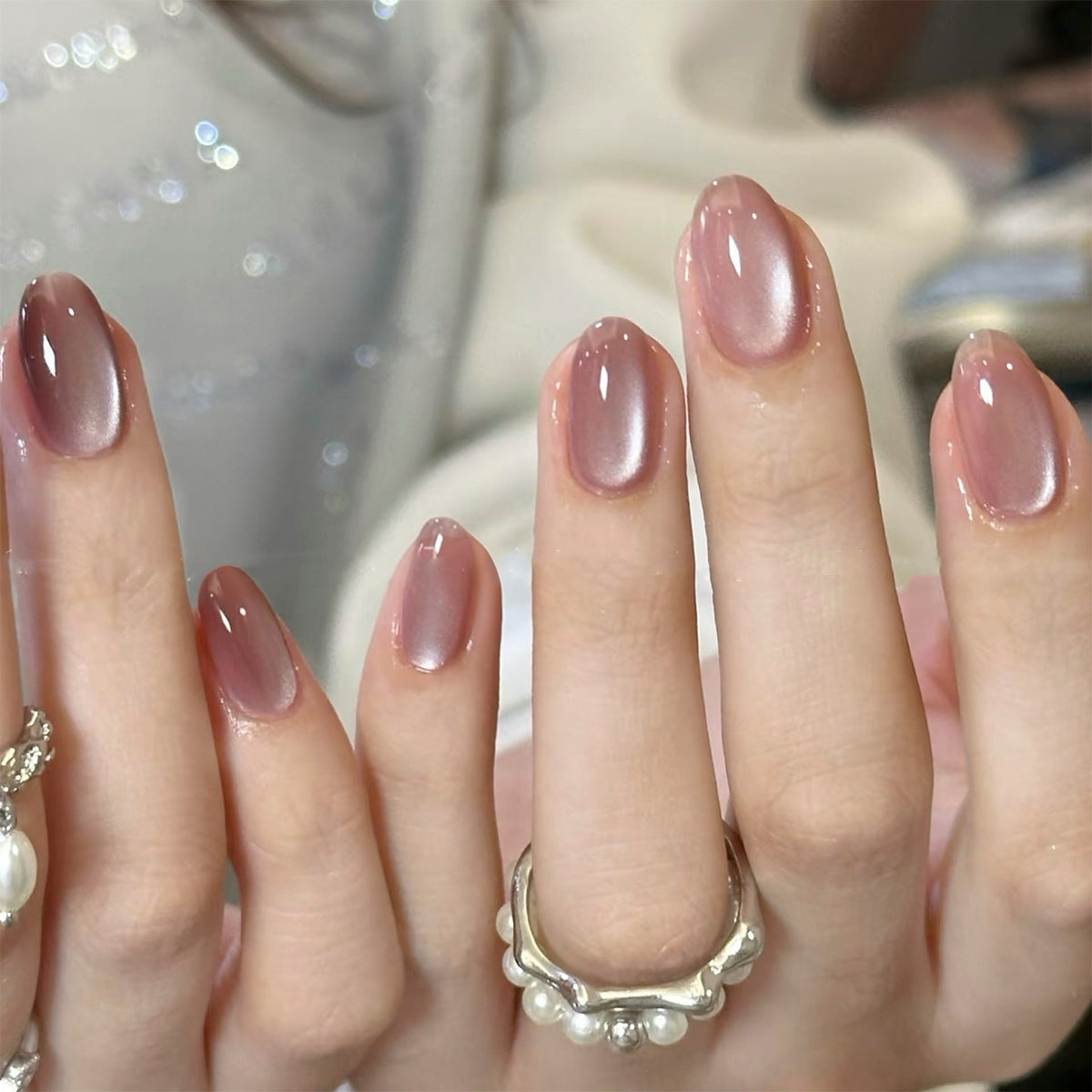 Close-up of a hand with pink nail polish and pearl jewelry.