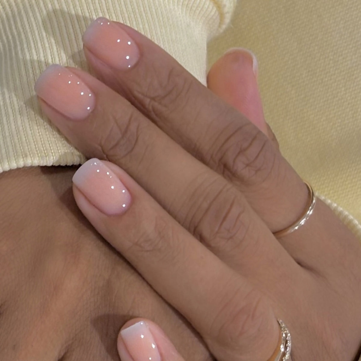 Close-up of a hand with pink nail polish and a gold ring on a light background