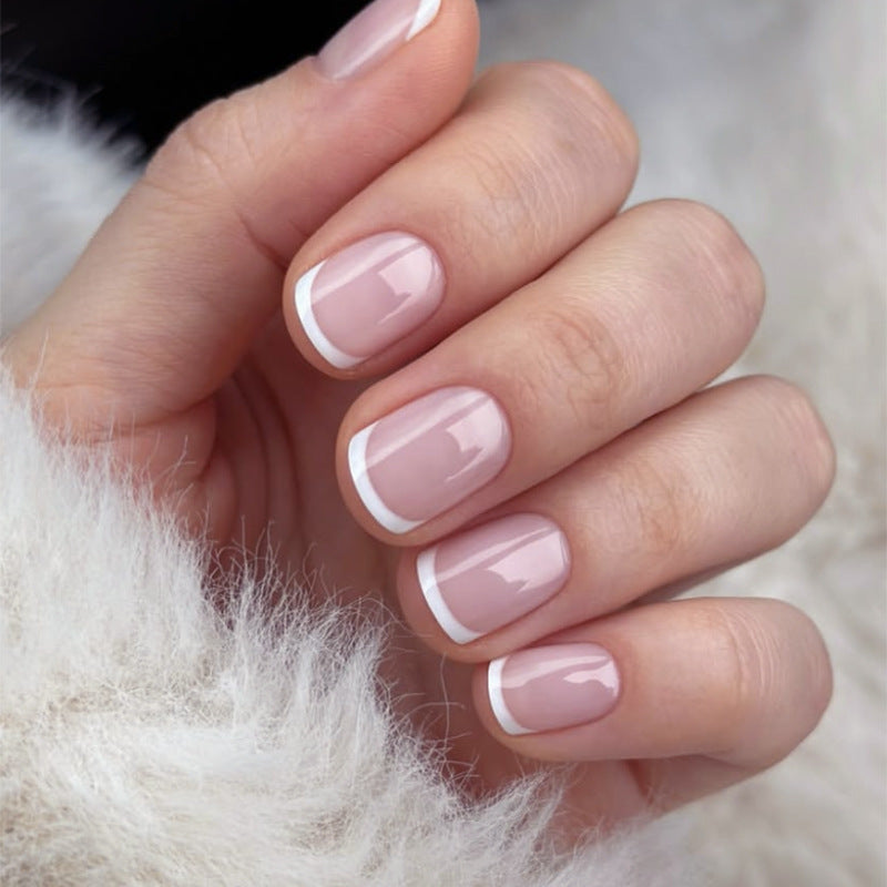 Close-up of a hand with pink nail polish and white tips on a soft, blurred background.