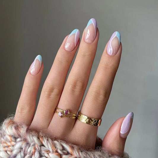 A hand with short oval pink nails with a groovy pattern, wearing gold rings, and resting on a textured surface.
