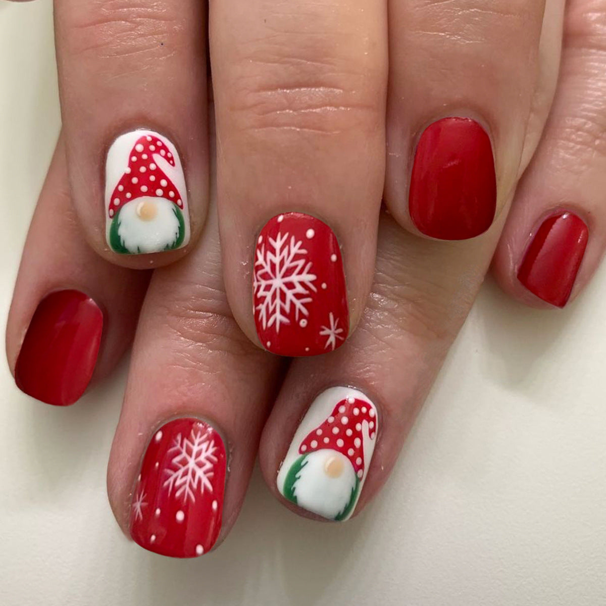 Nails with Christmas-themed designs including red snowflakes, white dots, and red hats with white pom-poms on a light background.