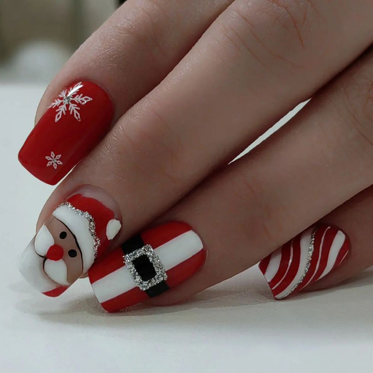 A set of red nails with a Christmas-themed design, featuring a cartoon depiction of Santa Claus and snowflakes.
