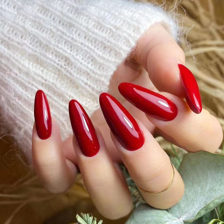 Cherry red almond-shaped press-on nails with a shimmer finish, displayed on a hand against a natural background.