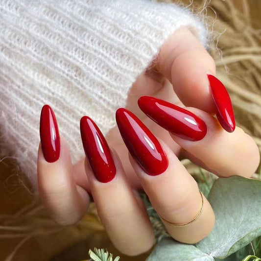 Cherry red almond-shaped press-on nails with a shimmer finish, displayed on a hand against a natural background.