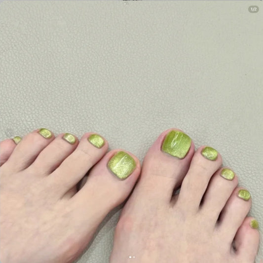A set of olive green press-on toenails with a glitter finish, displayed on a pair of feet.