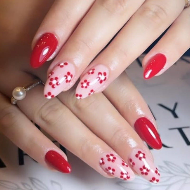 Close-up of a hand with red nail polish and floral designs on a blurred background