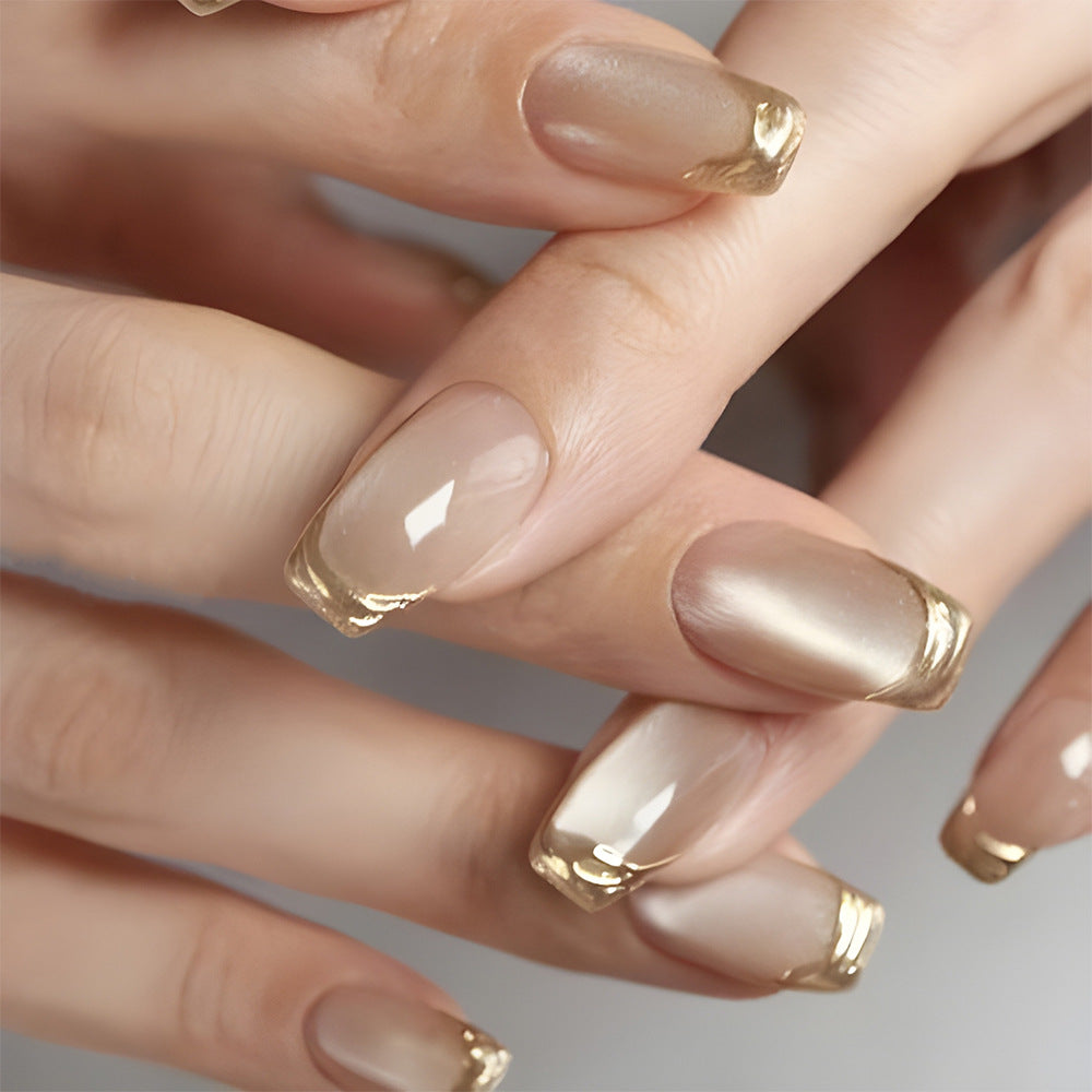 Close-up of hands with nude nail polish and gold accents on a neutral background