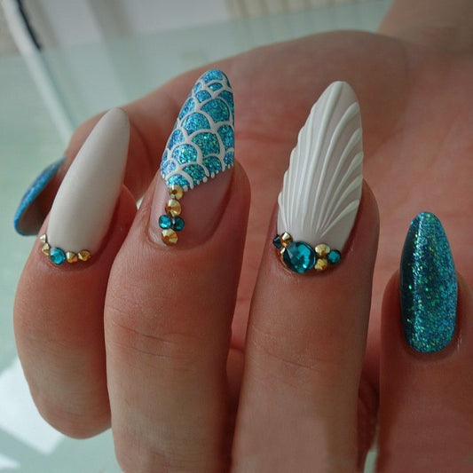 A set of long almond-shaped press-on nails with a shimmering teal and white design, adorned with jewel accents.