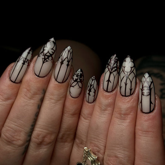 A set of long almond-shaped press-on nails with intricate black and white lace designs, displayed on a person's hands.