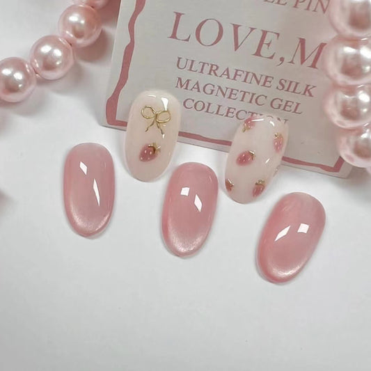 A set of soft pink magnetic gel press-on nails with floral blush and small bow designs, displayed alongside a strand of pearls and a card with the word 'LOVE'.