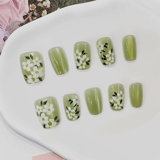 Green nail art with floral designs on a white surface