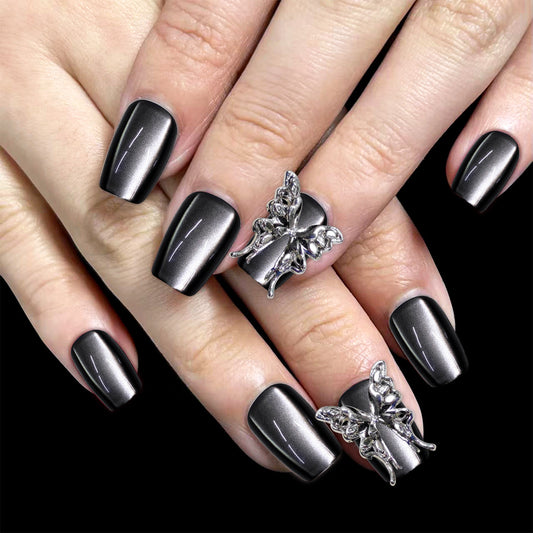 Close-up of a hand with black nail polish wearing silver butterfly rings on a black background