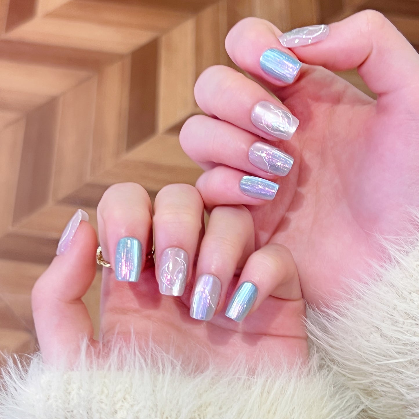 Close-up of hands with iridescent nail polish against a wooden background