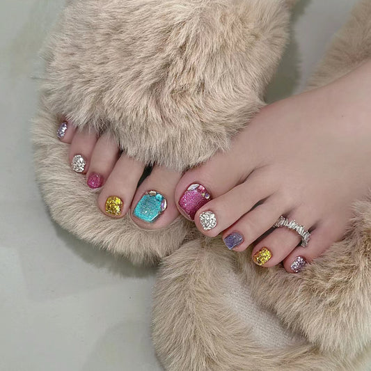 A set of colorful press-on toenails with glittering accents displayed on a pair of bear-patterned slippers.