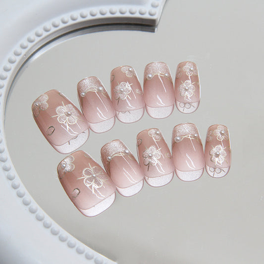 A set of pale pink press-on nails with glitter and floral accents, displayed on a reflective surface.