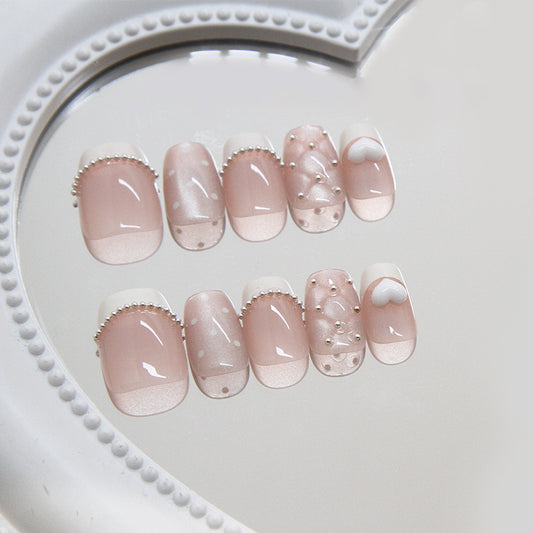 A set of long square pink press-on nails with shimmering pearls and whimsical designs, displayed on a white heart-shaped mirror.
