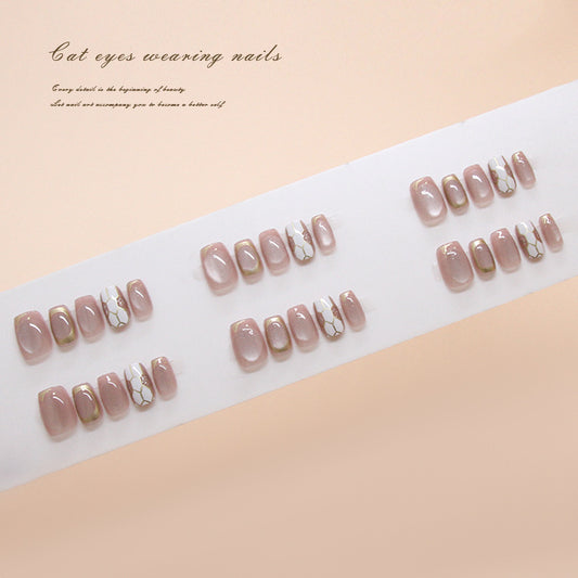 Set of press-on nails with a gold and white design on a white tray against a beige background.