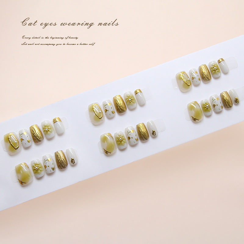 Press on nails with medium coffin shape featuring shimmery gold and cream colors and intricate floral designs.