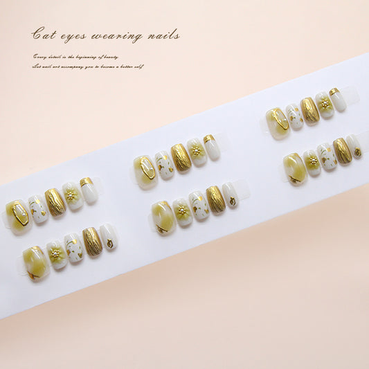 Press on nails with medium coffin shape featuring shimmery gold and cream colors and intricate floral designs.