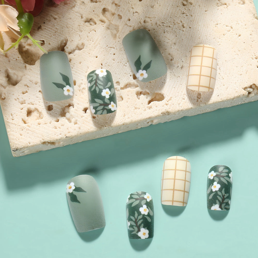 A set of long oval false nails with a sage green floral accent, laid out on a surface with a matte finish.