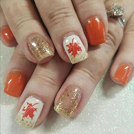 A set of press-on nails featuring a leaf design in orange and gold glitter on a medium square base.