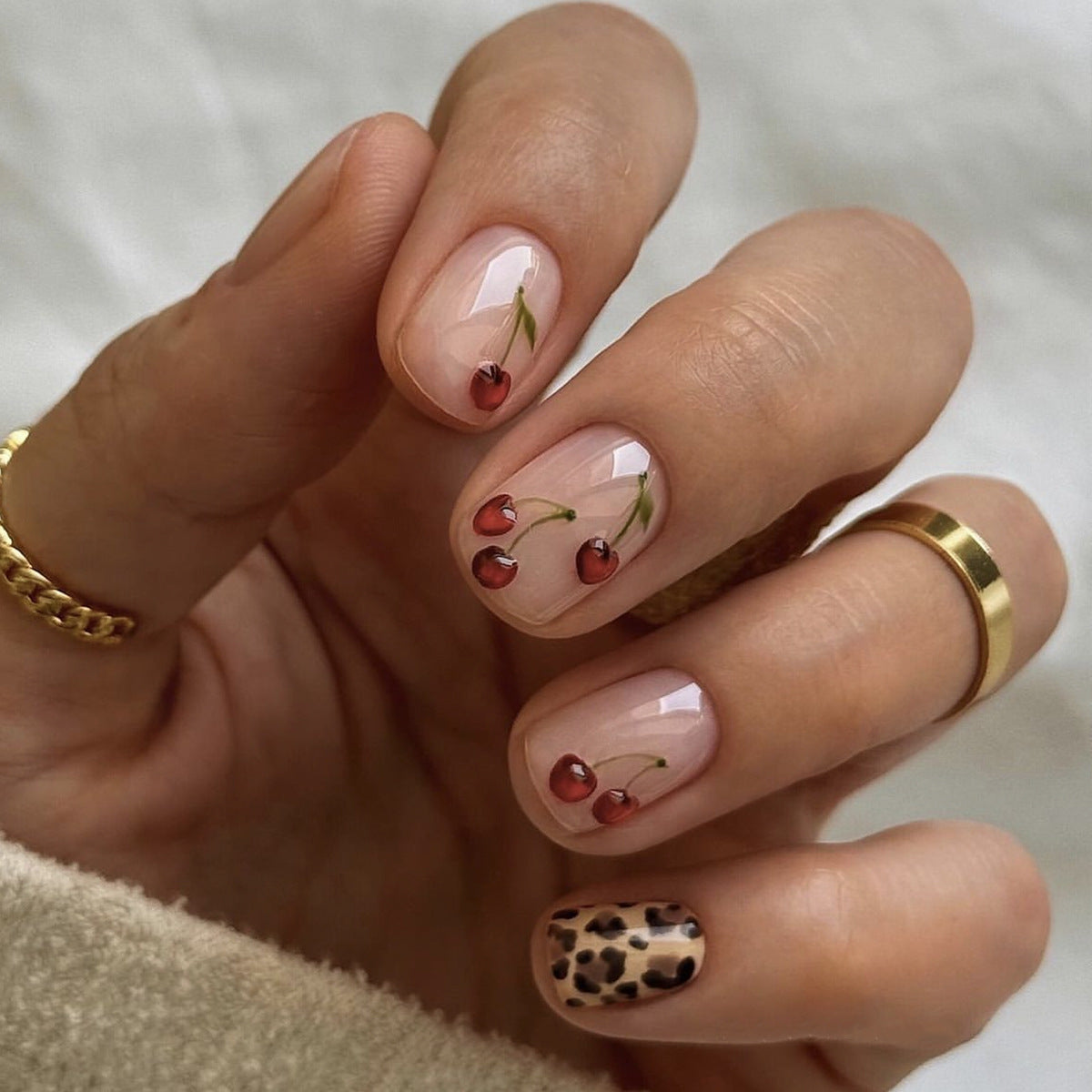 A set of beige press-on nails with delicate floral art and animal print accents, displayed on a hand.