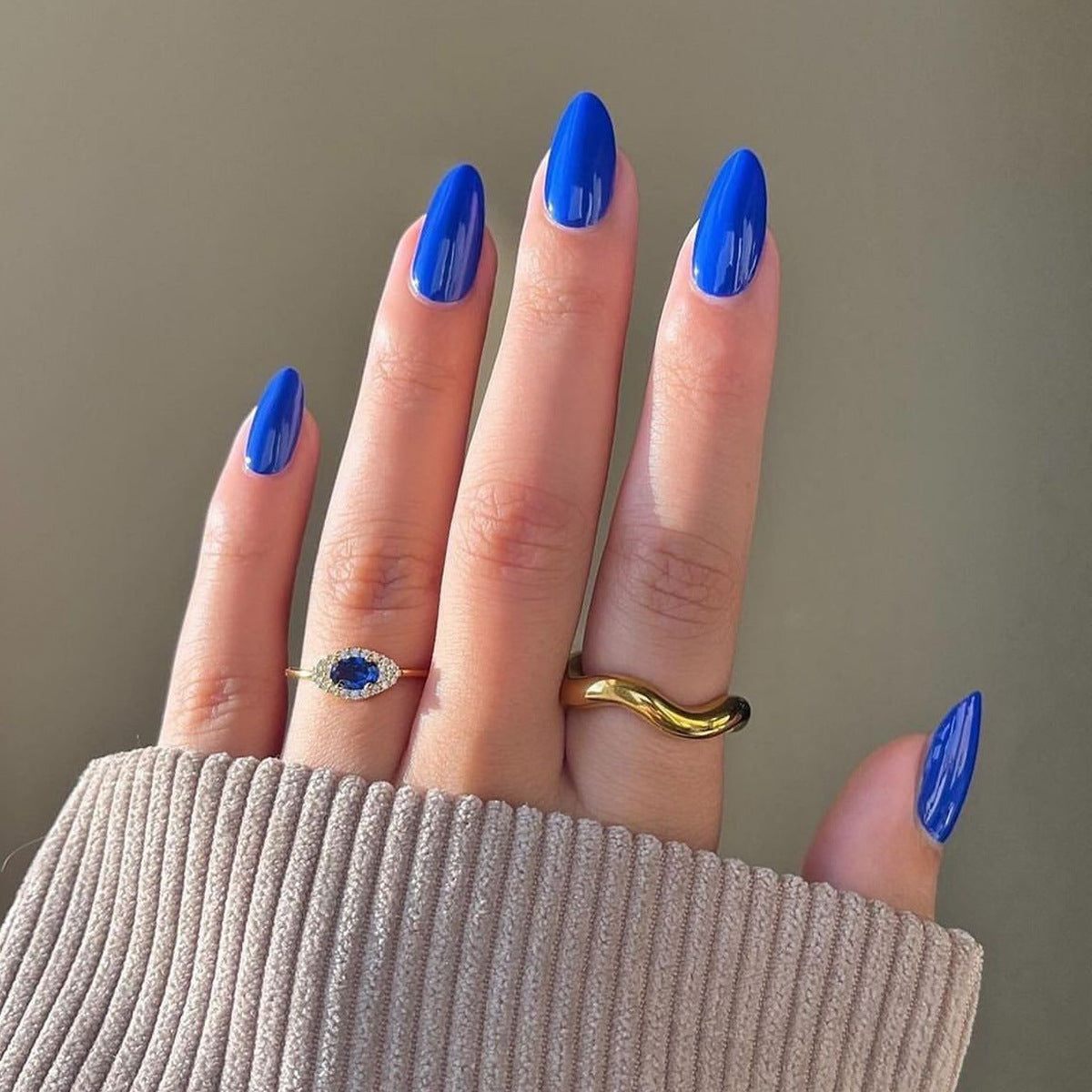 A hand with long almond shape royal blue press on nail set with glossy finish.