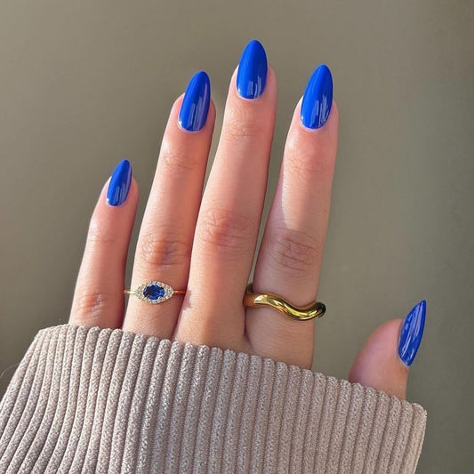 A hand with long almond shape royal blue press on nail set with glossy finish.