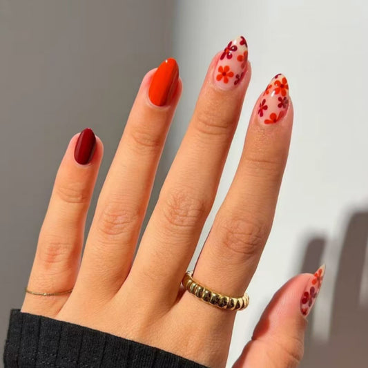A hand with medium almond orange and burgundy floral accent press on nails.