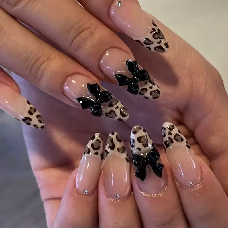 Chic Wildside Long Almond Beige Leopard Print Glossy Nails with Black Bow Accents and Rhinestone Detail