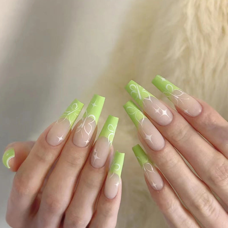 A set of long coffin-shaped nails in a spring green color with a floral art design.