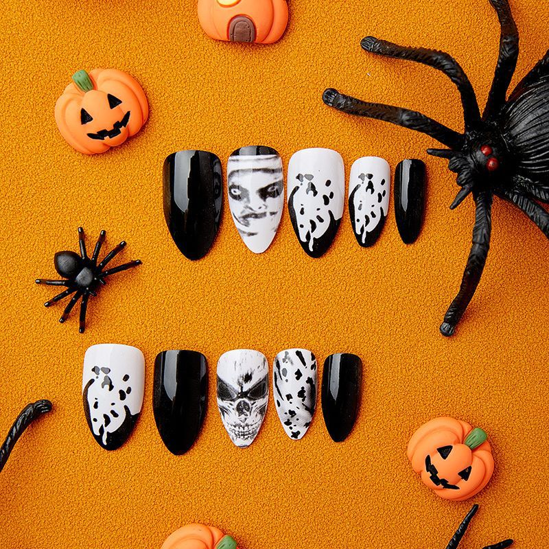 A set of press-on nails featuring black and white ghostly portraits, displayed on an orange background with Halloween-themed decorations around.