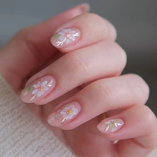 A set of press-on nails featuring a medium oval shape with a pale pink floral design, applied to a person's nails.