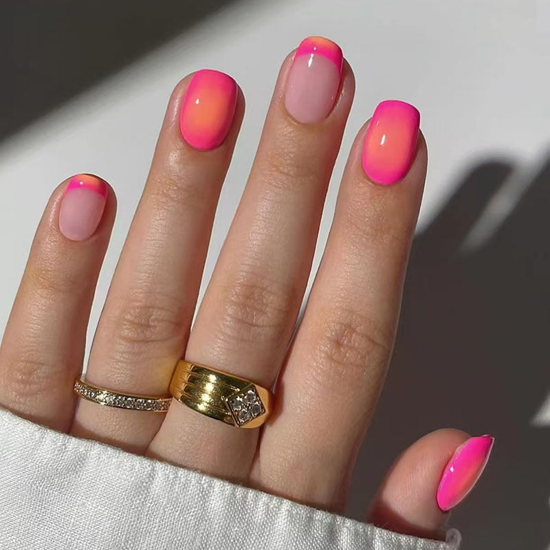 A set of press-on nails featuring a pink ombre design with a glossy finish, displayed on a hand with a ring on the finger.