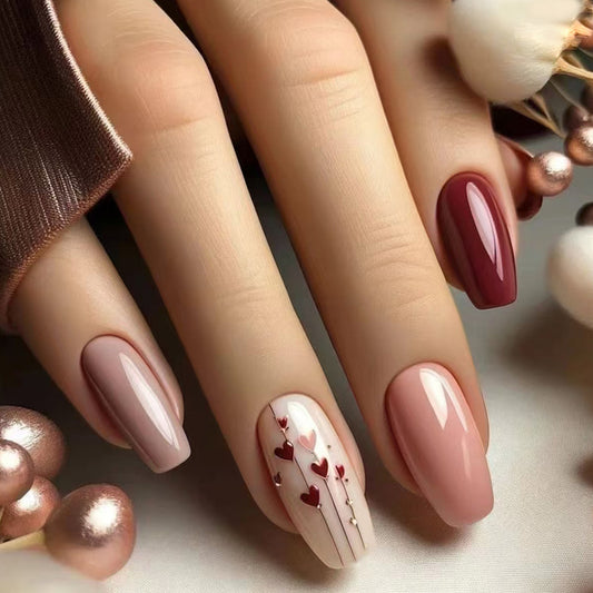 A set of long, coffin-shaped nails with a heart design, in shades of mauve and burgundy, shown resting on a surface with pearl-like decorations.
