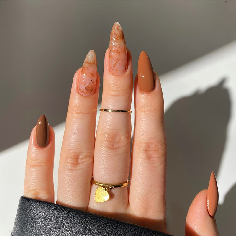 Hand with brown nail polish wearing two gold rings on a neutral background