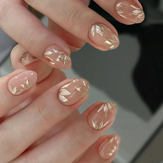 A set of blush pink press-on nails with a leaf design, displayed on a person's hands.