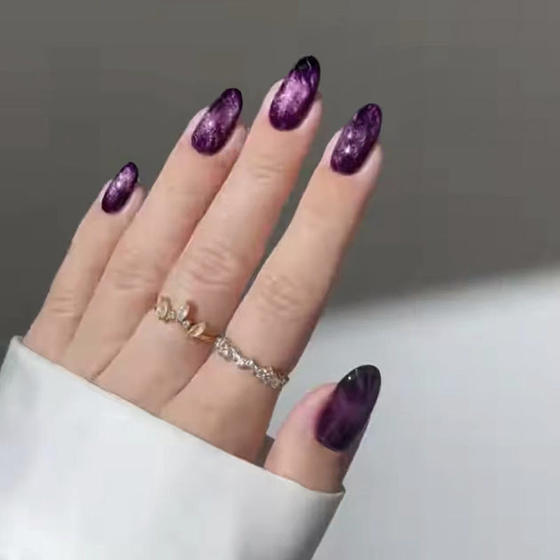 A person's hand with medium almond-shaped nails featuring a sparkling ombre finish in purple color.