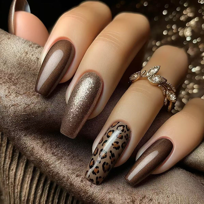 A set of long coffin-shaped nails in brown color with one nail featuring a leopard print accent.
