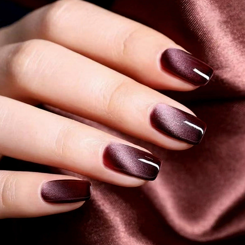 A close-up of a hand showcasing medium square-shaped nails with a burgundy ombre design and a high shine finish.